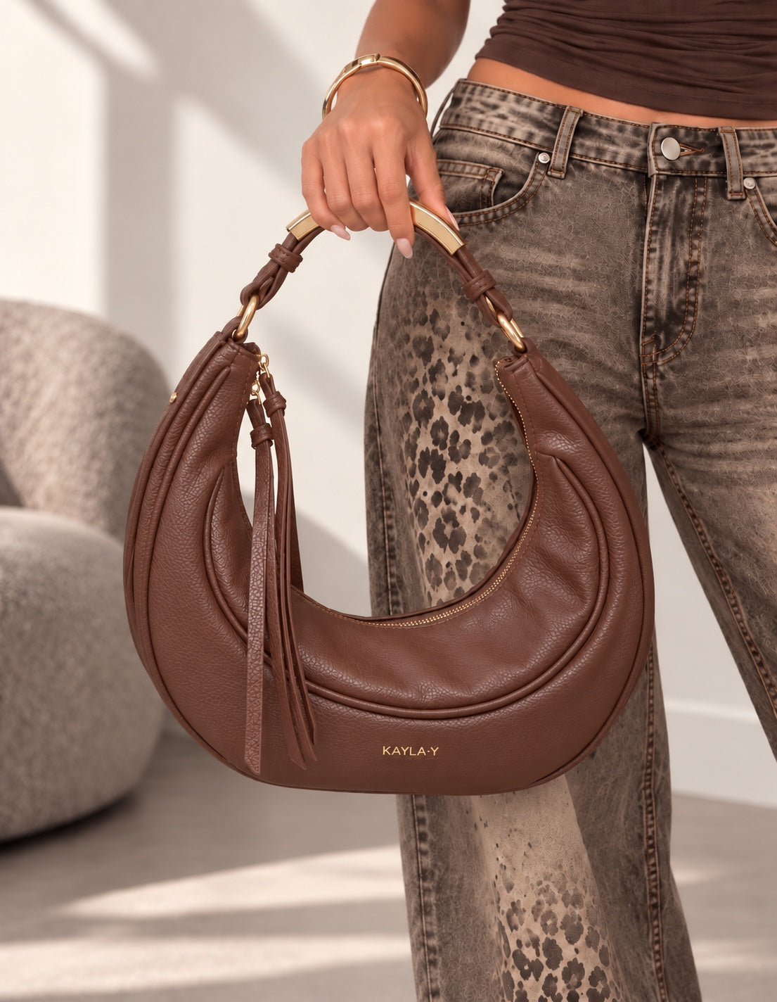 Borsa Ella marrone a mezzaluna con dettagli dorati, tenuta a mano dalla modella